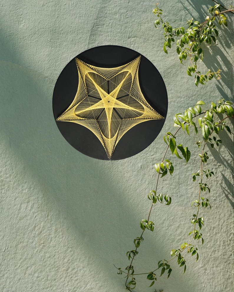 May include: A circular wall art piece featuring a black background with a geometric star pattern created from yellow string. The design consists of intricate, intersecting lines that form a five-pointed star shape, anchored by small pins.