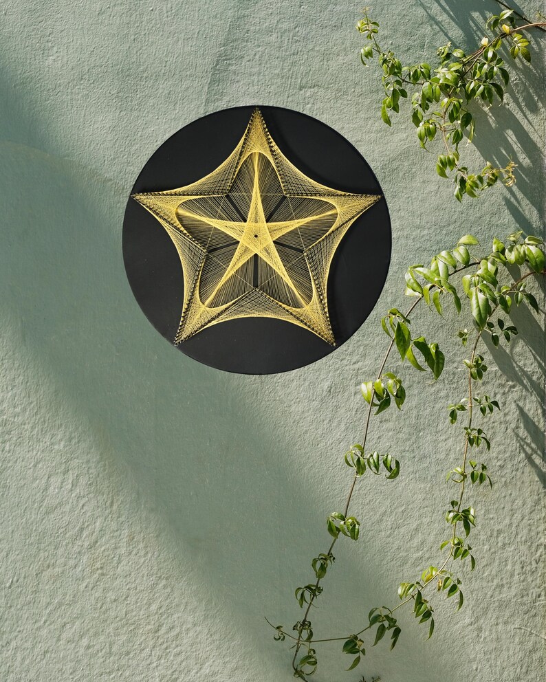 May include: A circular black wall art piece featuring a five-pointed star design created with yellow string art. The yellow threads are tightly wound around small nails to form geometric patterns, contrasting against the solid black background.