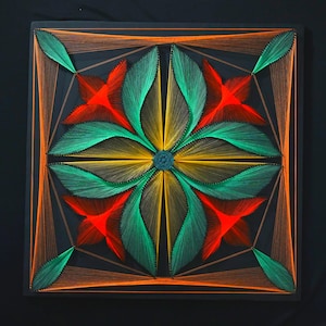 Peut inclure: Une œuvre d'art en fils tendus de forme carrée sur un panneau noir, présentant un motif floral symétrique réalisé avec des fils orange, jaunes et verts vifs. Le design rayonne depuis un point central, formant des pétales et des bordures.
