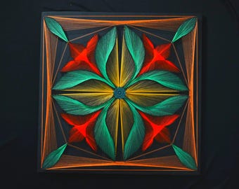 May include: A square string art piece on a black board featuring a symmetrical floral pattern created with vibrant orange, yellow, and green threads. The design radiates from a central point, forming petal-like shapes and geometric borders.