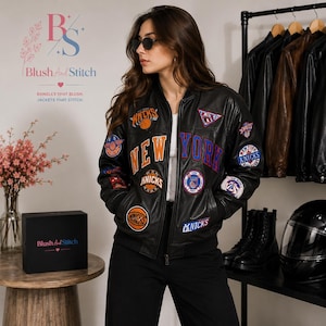 May include: A black leather bomber jacket featuring various New York Knicks basketball team patches in orange, blue, and white. The jacket has a front zipper closure, ribbed cuffs, and bold lettering across the chest. It is worn over a white shirt.