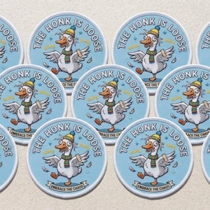 Op de afbeelding: Tien ronde stickers met een cartoon gans die een kleurrijke gebreide muts en sjaal draagt. De gans heeft een pleister op de vleugel. De tekst luidt THE HONK IS LOOSE en EMBRACE THE CHAOS op een lichtblauwe achtergrond met kleine zwevende veren.