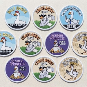 Könnte beinhalten: Eine Sammlung von zehn runden bestickten Aufnähern mit Gänse-Motiven. Die Designs zeigen eine Gans mit Messer, eine Gans in Toilettenpapier eingewickelt, eine Gans im Arztkittel, eine Gans mit Krone auf Goldmünzen und eine Gans mit einem Kompass.