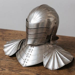 Op de afbeelding: Een gepolijste stalen helm met een meerlaags vizier en een halsstuk met waaiervormige schouderplaten. Het metalen pantser bevat een donkerbruine leren riem met een gesp aan de zijkant en zichtbare klinknagels langs de gebogen nek- en borstsecties.