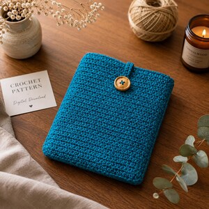 Può includere: Una custodia rettangolare all'uncinetto color verde acqua con un singolo bottone in legno al centro superiore. Un cartoncino bianco con il testo CROCHET PATTERN Digital Download è visibile accanto alla custodia, realizzata con un punto denso.