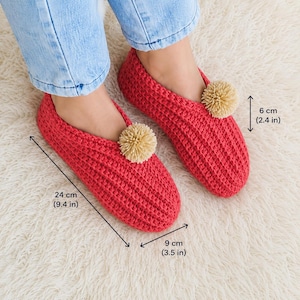 May include: A pair of red crochet slippers featuring a beige pom-pom on each top. The slippers measure 9.4 inches in length, 3.5 inches in width, and 2.4 inches in height, as indicated by the visible measurement labels on the image.