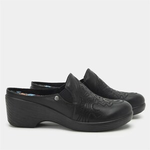 May include: A pair of black leather clogs with a decorative embossed design on the vamp. The clogs have a low wedge heel and a floral patterned insole. The shoes are designed for comfort and style.