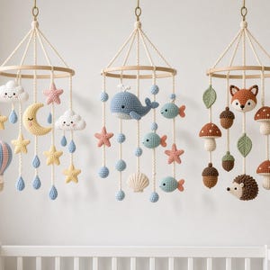 May include: Three hanging crochet mobiles suspended from wooden hoops. The first features a hot air balloon, clouds, stars, and a moon. The second displays a whale, fish, starfish, and seashell. The third includes a fox, hedgehog, mushrooms, acorns, and leaves.