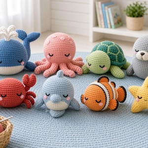 Könnte beinhalten: Eine Sammlung von acht gehäkelten Stofftieren aus dem Meer, darunter ein blauer Wal, ein rosafarbener Oktopus, eine grüne Schildkröte, eine graue Robbe, ein roter Krebs, ein hellblauer Delfin, ein orange-weißer Clownfisch und ein gelber Seestern.