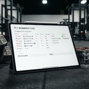 Può includere: Un tablet che mostra un registro di allenamento digitale intitolato 1. WORKOUT LOG con colonne per data, esercizio, serie, ripetizioni, peso e stato. Lo schermo mostra le voci per squat con bilanciere, panca piana e stacchi da terra.