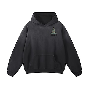 Puede incluir: Una sudadera con capucha negra que cuenta con un bolsillo tipo canguro frontal y mangas largas. En la parte superior izquierda del pecho, hay un pequeño gráfico de una figura sentada en posición de meditación sobre el texto negro SPIRITUAL - IT.