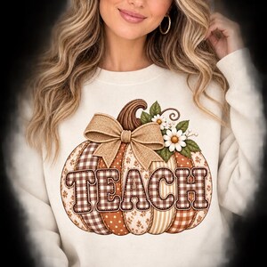May include: A cream-colored crewneck sweatshirt featuring a large graphic of a pumpkin with the word TEACH printed across it. The pumpkin has segments with brown and white gingham, polka dot, and floral patterns, topped with a burlap bow and daisies.