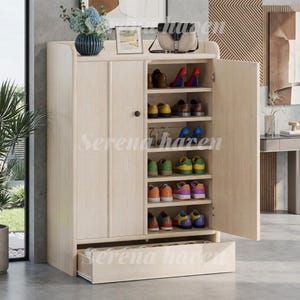 May include: A light wood shoe cabinet with two doors and a bottom drawer. The interior features six shelves holding various pairs of shoes, including heels, sneakers, and flats. A blue vase with flowers and a small framed picture sit on top.