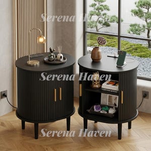 May include: Two black oval bedside tables with vertical fluted detailing and gold handles. The left table features a gold lamp and decorative items. The right table has an open shelf containing books, a clock, and crystals, with a phone on top.
