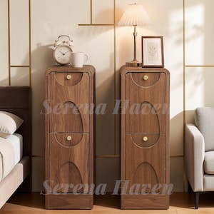 May include: Two tall, narrow wooden storage cabinets with a dark walnut finish. Each unit features two stacked doors with arched, recessed panel detailing and small, round, gold-toned metal knobs centered on the upper portion of each door panel.