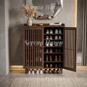 May include: A dark wood shoe cabinet featuring vertical slatted doors, one of which is open to reveal multiple interior shelves filled with various pairs of shoes. The cabinet stands on four short legs and has a flat top surface holding a vase.