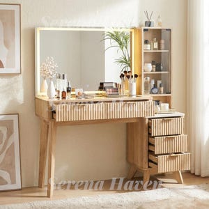 May include: A light wood vanity table featuring a rectangular LED-lit mirror, a wide drawer with a fluted front, and a side cabinet with three matching fluted drawers and an upper glass-door shelf unit containing various cosmetic bottles and jars.
