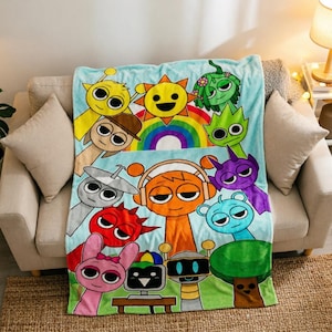 May include: A light blue fleece blanket featuring a colourful graphic print of various cartoon characters, including a yellow sun, a rainbow, and diverse creatures in shades of orange, pink, red, purple, green, and grey, with large expressive eyes.
