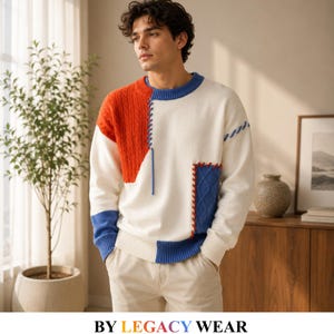 Puede incluir: Un suéter de manga larga con un diseño de bloques de color en blanco, naranja y azul. La prenda incluye paneles de punto trenzado, un cuello redondo acanalado y detalles de costuras decorativas. El texto BY LEGACY WEAR aparece abajo.
