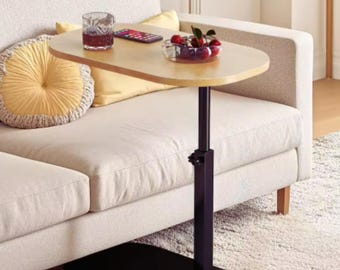 May include: A height-adjustable side table with a light wood-toned oval top and a black metal base. The table features a central vertical support column with a manual adjustment knob, positioned on a flat, oval-shaped black floor base.