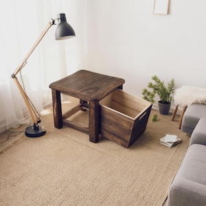 May include: A dark brown wooden side table with a square top and four sturdy legs. A matching wooden storage crate with cutout handles is partially pulled out from underneath the table, revealing a light-colored interior wood finish.