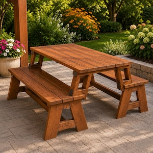 May include: A brown wooden picnic table with an attached bench on each side. The table features a rectangular top made of horizontal planks and sturdy A-frame legs. The wood has a visible grain pattern and a warm, medium-toned finish.