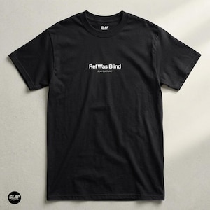 May include: A black short-sleeve t-shirt featuring the white text Ref Was Blind and SLAPCULTURE printed on the chest. The shirt has a crew neckline and a small SLAP logo printed on the inside of the collar area, centered on the upper chest.