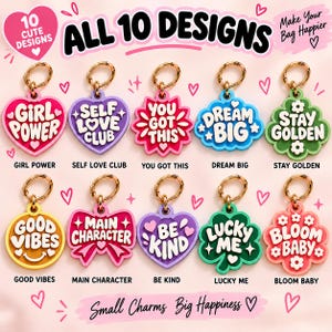 May include: Ten colorful acrylic bag charms with gold-tone metal rings. Designs include heart, flower, and bow shapes with phrases like Girl Power, Self Love Club, You Got This, Dream Big, Stay Golden, Good Vibes, Main Character, Be Kind, Lucky Me, and Bloom Baby.