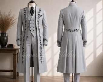 May include: A light gray three-piece suit featuring a long coat, a double-breasted vest, and trousers. The coat and vest are adorned with black floral embroidery along the lapels and cuffs. A black necktie is worn with a white collared shirt.
