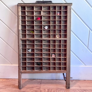 May include: A rectangular wooden printer's tray featuring numerous small, square compartments arranged in a grid. Several tiny, colorful animal-shaped figurines are placed sporadically within the individual slots of the wooden display case.