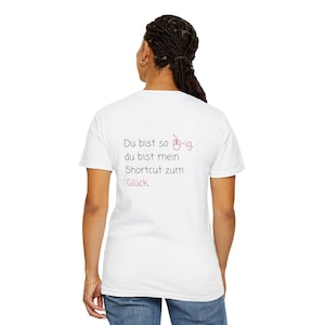 Könnte beinhalten: Ein weißes T-Shirt mit kurzen Ärmeln und einem schwarzen sowie rosafarbenen Text auf der Rückseite: Du bist so [Maus-Symbol]-ig, du bist mein Shortcut zum Glück. Das T-Shirt wird mit einer blauen Jeans kombiniert und wirkt schlicht.
