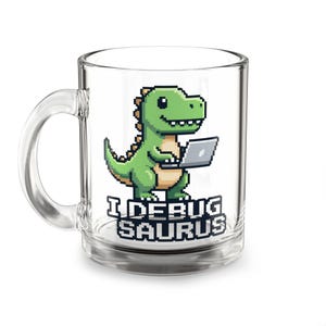 May include: A clear glass mug featuring a pixel art graphic of a green dinosaur holding a laptop. Below the dinosaur, the text reads I DEBUG SAURUS in a bold, pixelated font. The mug has a standard handle and a smooth, transparent finish.