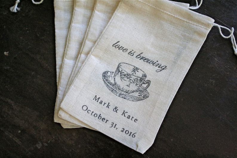 May include: Set of six small, off-white fabric bags with a drawstring closure. Each bag has a black and white illustration of a teacup and the text "love is brewing" and "Mark & Kaite October 31, 2016".