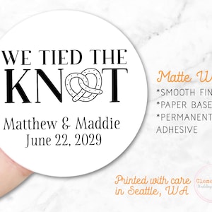 Round label is shown stuck on a fingertip.  Overlay text: ‘Matte White: Smooth finish, paper based, permanent adhesive. Printed with care in Seattle WA by Clementine Wedding & Party.'