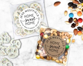May include: Two cellophane bags filled with snacks. One contains white chocolate-covered pretzels with sprinkles, and the other has a mix of nuts and candies. Both bags have a round sticker that reads "JESS WESTFIELD HOME sweet HOME SEATTLE REALTY GROUP 206.555.1234."