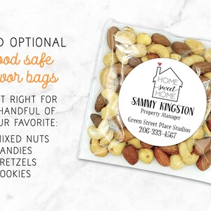 Square clear treat bag shown filled with mixed nuts.  Bag has a round white label attached.  Label design: 'Home Sweet Home' inside a simple house outline, with a small red heart coming out of the chimney.  Labels are personalized at the bottom with professional contact info Name/Title/Company/Phone#/Email.  Overlay text: 'Add optional food safe favor bags - just right for a handful of your favorite mixed nuts, candies, pretzels, cookies.'
