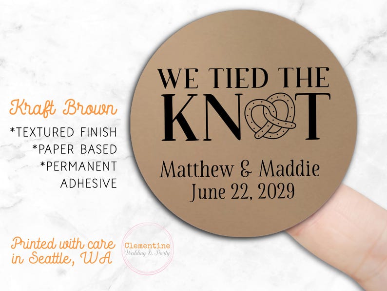 Round label is shown stuck on a fingertip.  Overlay text: 'Kraft Brown: Textured finish, paper based, permanent adhesive. Printed with care in Seattle WA by Clementine Wedding & Party.'