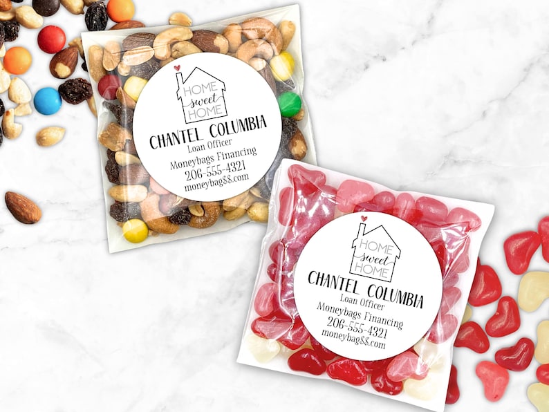 Two clear treat bags shown, one filled with trail mix and the other with red and pink heart shaped candies.  Each bag has a round white label attached.  Label design: 'Home Sweet Home' inside a simple house outline, with a small red heart coming out of the chimney.  Labels are personalized at the bottom with professional contact info Name/Title/Company/Phone#/Email.