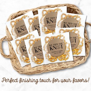 A basket is filled with favor bags.  Each clear bag is filled with brown pretzels and has a kraft paper label attached to the front.  One clear favor bag filled with pretzels has a round brown label attached.  Label has text 'We tied the KNOT' with the O replaced by a cute pretzel graphic.  Labels are personalized below the design with names and wedding date.  Overlay text: 'Perfect finishing touch for your favors!'