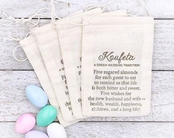 May include: Five small white bags with brown drawstring closures, each containing five sugared almonds. The bags are stacked on a white wooden surface. The bags have a brown inscription that reads "Koufeta A Greek Wedding Tradition Five sugared almonds for each guest to eat to remind us that life is both bitter and sweet. Five wishes for the new husband and wife -- health, wealth, happiness, children, and a long life!"