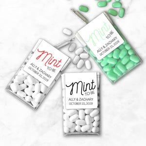 May include: Three clear plastic boxes filled with mints, each with a label that reads "Mint to Be" and the names "Ally & Zachary" with the date "October 22, 2029." One box contains white mints, another green, and the third white.