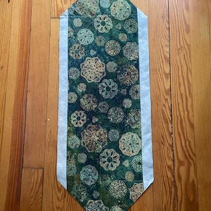 May include: A green table runner with a white border and a pattern of gold Celtic knots.