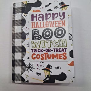 Könnte beinhalten: Ein rechteckiges Notizbuch mit einem schwarz-weiß karierten Buchrücken und einem weißen Einband, der mit Illustrationen von Hexen, Spinnen und Spinnennetzen verziert ist. Der Text in der Mitte lautet: Happy Halloween, BOO, WITCH, TRICK-OR-TREAT, COSTUMES.