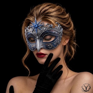 May include: A masquerade mask featuring a deep blue celestial pattern with silver filigree detailing. The mask is adorned with a prominent central blue star-shaped emblem at the forehead and smaller star accents throughout the intricate frame.