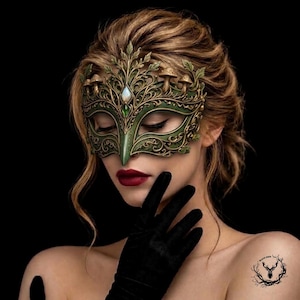 May include: An ornate masquerade mask in shades of forest green and antique gold, featuring intricate filigree, sculpted mushroom accents, and a central iridescent gemstone. The mask covers the upper face, showcasing detailed leaf motifs and scrollwork.