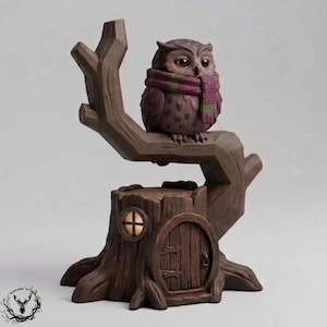 Könnte beinhalten: Eine braune Eulenfigur mit einem violett-grün gestreiften Schal, die auf einem braunen Ast sitzt, der aus einem Baumstumpf ragt. Der Stumpf hat eine kleine gewölbte Holztür und ein rundes Fenster, aus dem ein warmes Licht nach außen scheint.