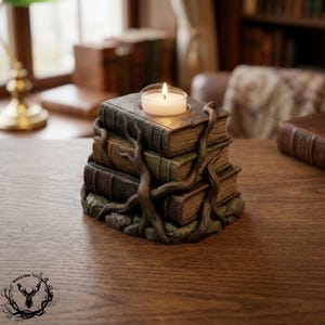 May include: A decorative candle holder shaped like a stack of three weathered, antique-style books bound together by sculpted brown tree roots. A small, round white tea light candle with a lit flame sits in a circular indentation on the top book.