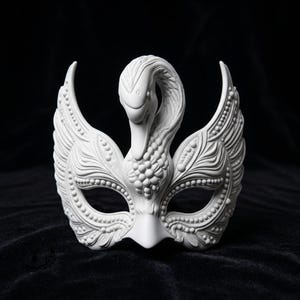 May include: A matte white masquerade mask featuring a sculpted swan head at the center. The mask is adorned with intricate raised beadwork and feather-like patterns extending outward to form the eye openings and side wings.