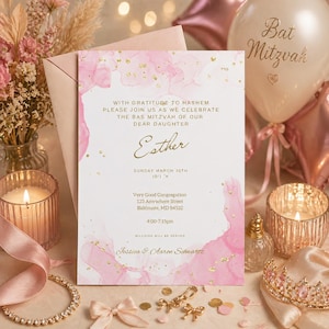 Peut inclure: Une invitation de Bat Mitzvah avec des accents d'aquarelle rose et des détails dorés. L'invitation comprend le nom "Esther" et les détails de l'événement. Éléments décoratifs : bougies, ballons et couronne ornée de bijoux.