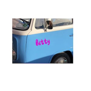 Puede incluir: Una furgoneta vintage azul con techo blanco y una calcomanía rosa "Betty" en el lateral.